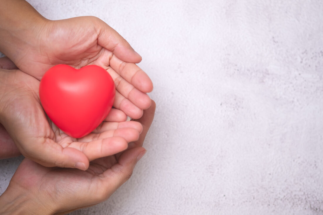 Two pairs of hands gently holding a red heart
